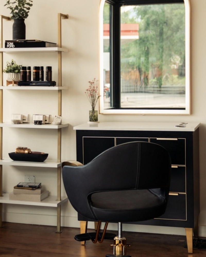 A black and brass styling chair before the arched mirror at Rise Above Beauty Lounge