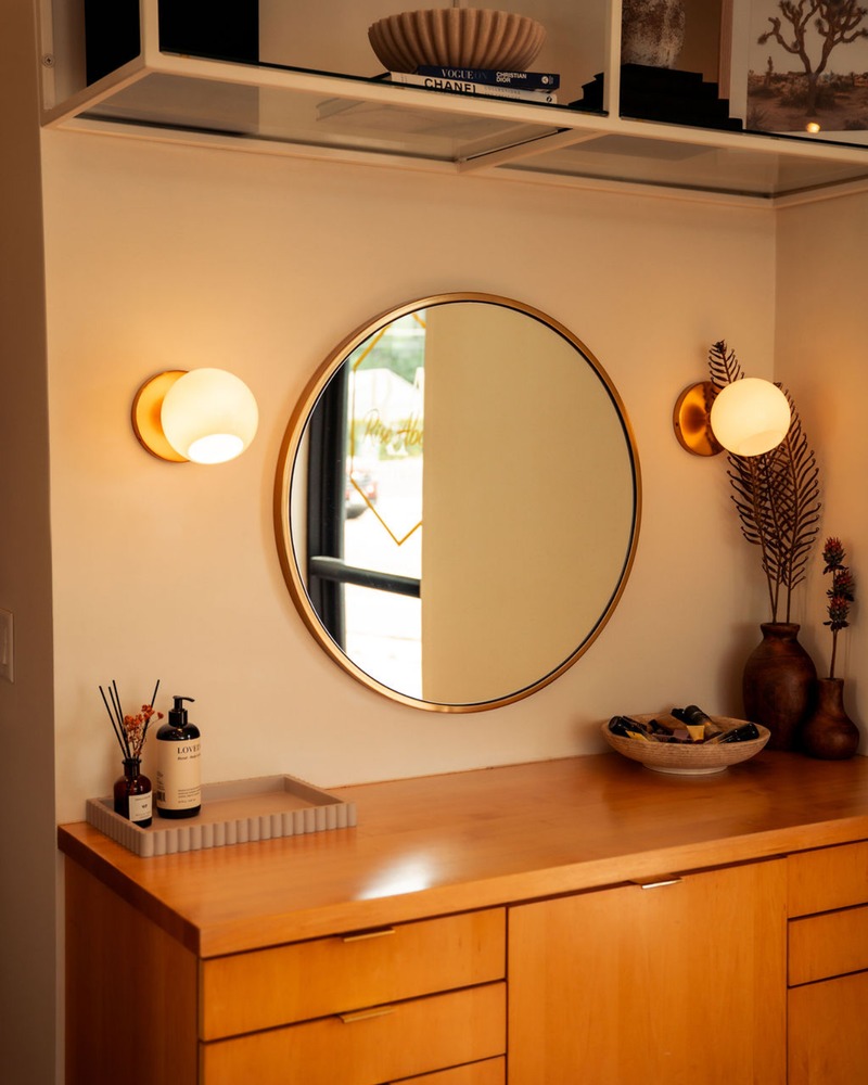 The round brass mirror and warm wood vanity at Rise Above Beauty Lounge