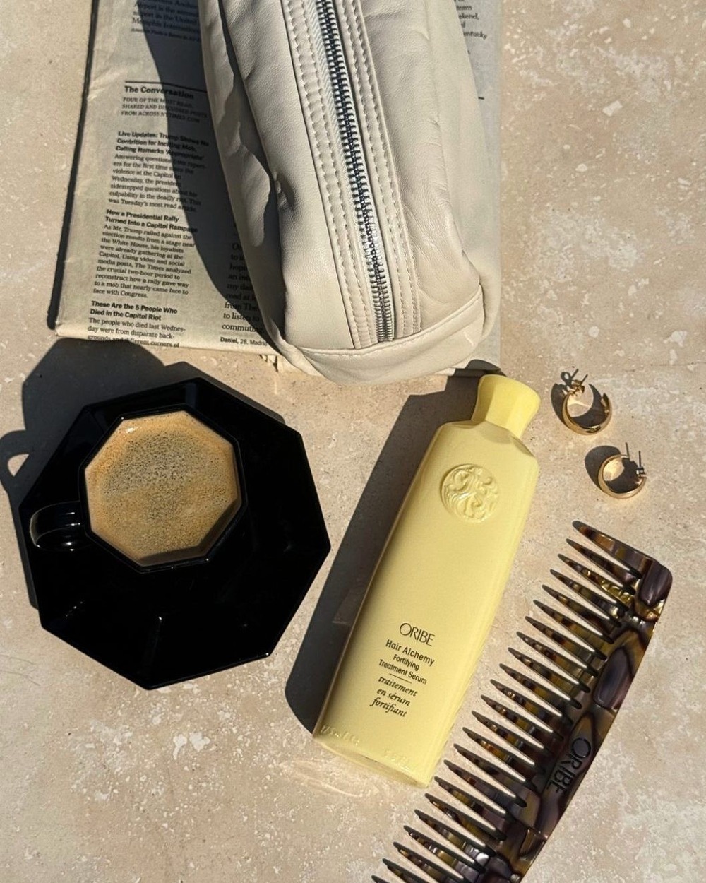 Oribe Hair Alchemy serum with an Oribe comb and gold earrings